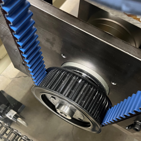Close-up of a blue toothed timing belt installed on a black pulley within an industrial power transmission system, showing precise alignment and tension.
